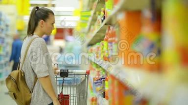令人惊叹的年轻布鲁内特女士与购物车购买一些饮料在超市站在货架附近与果汁。